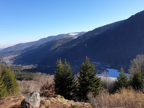 Vue panoramique sur les Vosges et le lac d’Alfeld, entouré de forêts et de collines verdoyantes.