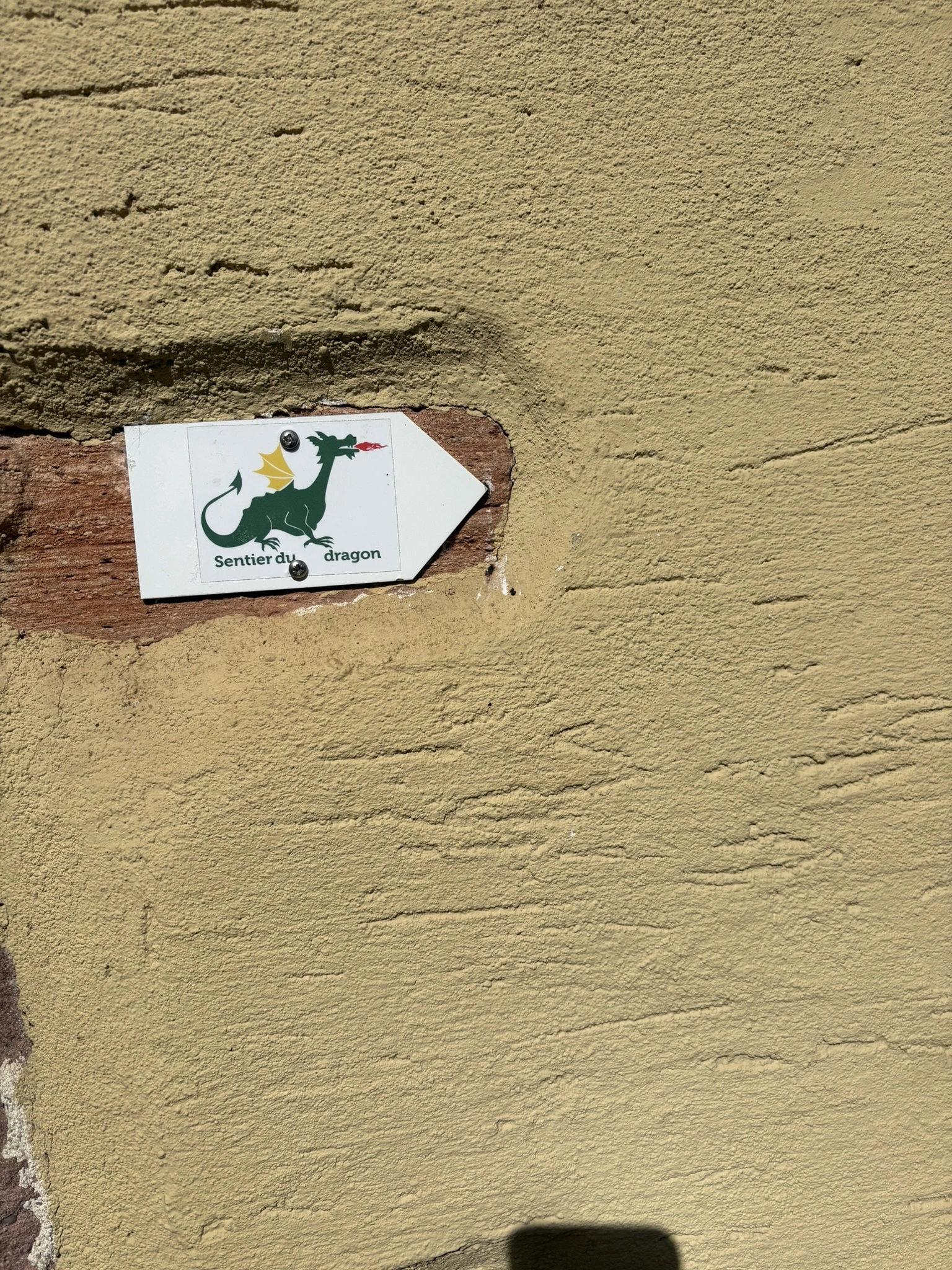 Panneau directionnel indiquant le sentier du Dragon au cœur du centre historique de Turckheim en Alsace.